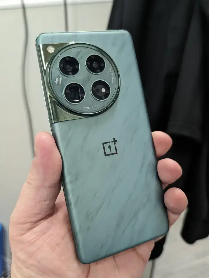 The OnePlus 12 smartphone in emerald green colorway displaying the front and back design. The front shows the edge-to-edge display with hole-punch camera. The back shows the Quad camera module and OnePlus branding.