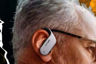 A man wearing Olive Max wireless earbud hearing aids - sleek white/black earbuds in ears. Earbuds have a wraparound your ear design.