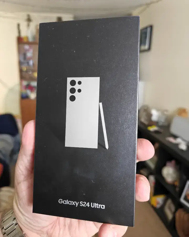 Unboxing experience of the Samsung Galaxy S24 Ultra smartphone in Orchid Gray color, showcasing the phone and its packaging elements.