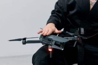 Person in a black robe handling a drone on lap in a studio setting.