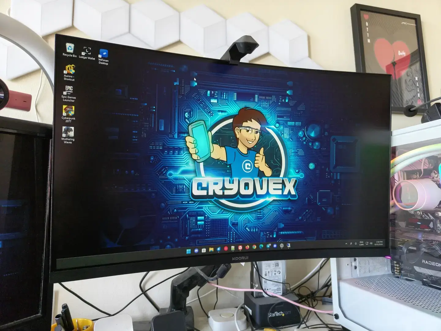 KOORUI 27E6CA curved gaming monitor mounted on a swivel arm in a CRYOVEX desktop setup, displaying a colourful Windows desktop.