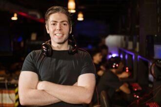 Smiling gamer standing with headphones in an illuminated gaming arena.