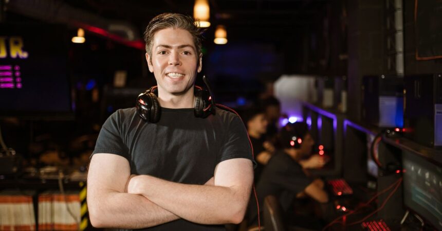 Twitch CEO Speculates on GTA 6 Online Release Window | Smart Tech, Sharp Takes - CRYOVEX.com Smiling gamer standing with headphones in an illuminated gaming arena.