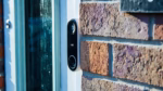 Close-up of a modern white smart video doorbell mounted on a brick wall
